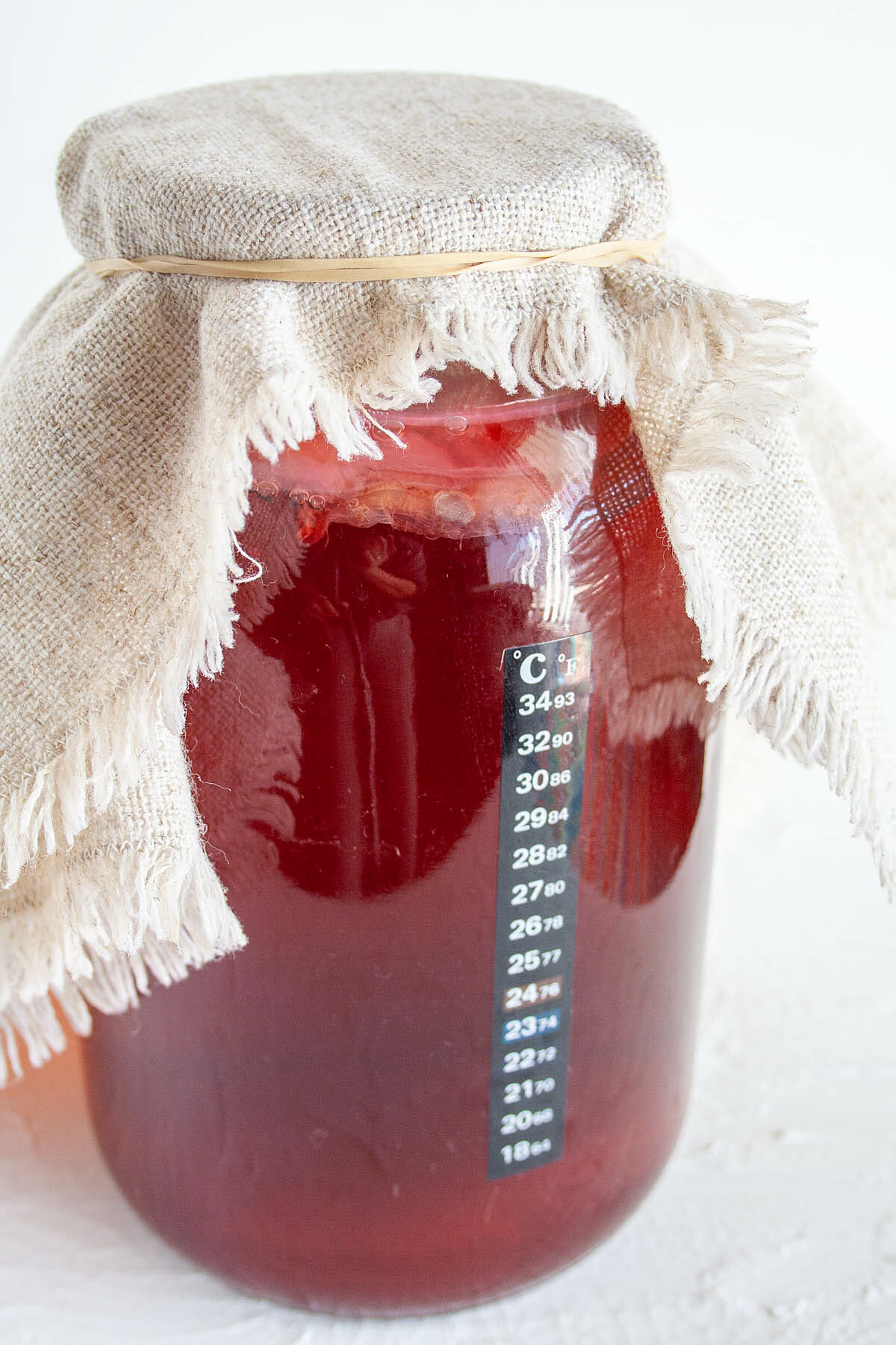 Hibiscus Kombucha in a gallon-sized jar with towel secured on top.