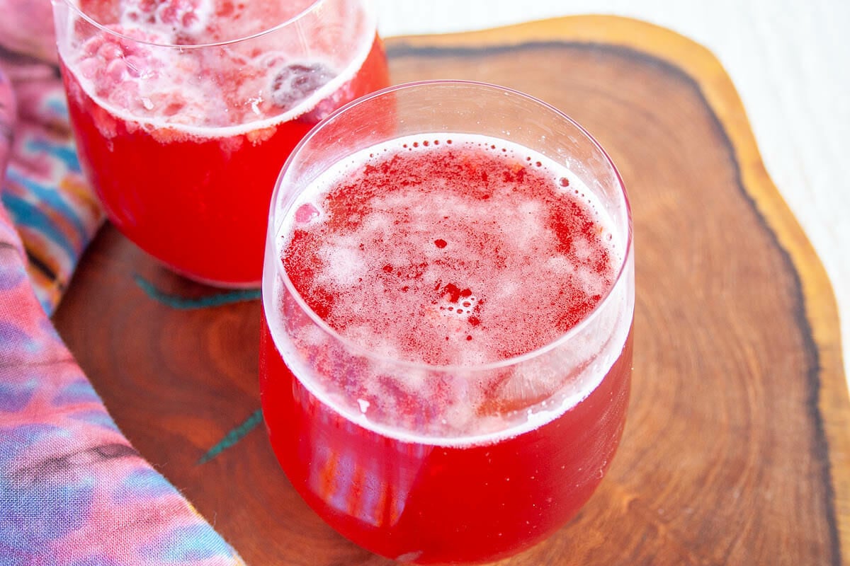 Mixed Berry Hibiscus Kombucha in wine glasses on cutting board.