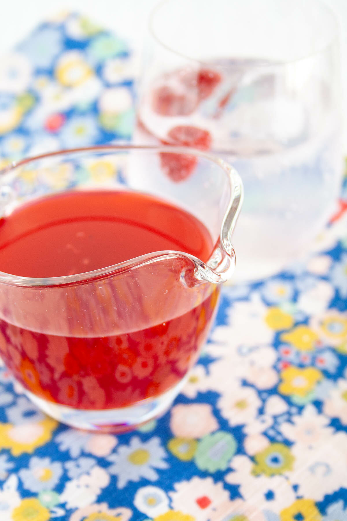 Raspberry Shrub in a pitcher with glassful of club soda in the background.