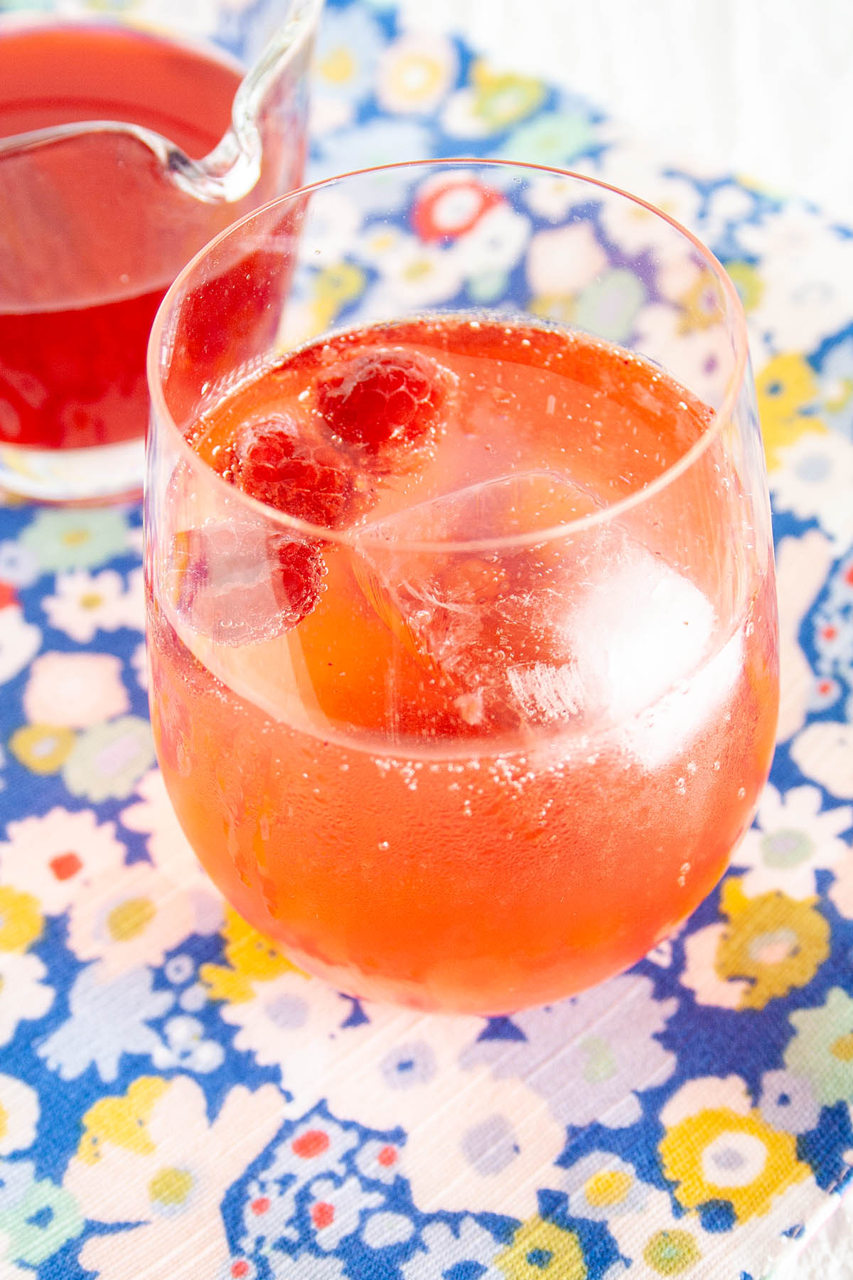 Raspberry Shrub and club soda in a glass with pitcher of shrub in background.