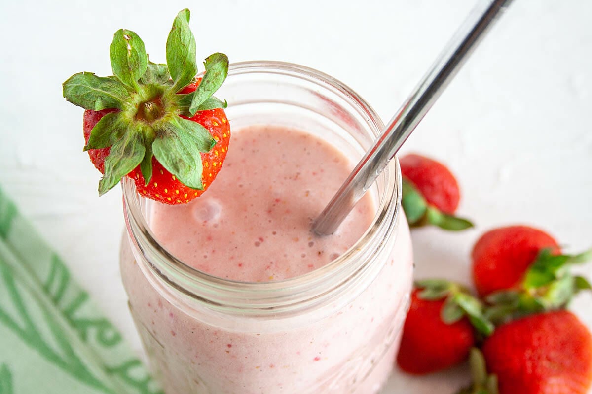 Vegan Strawberry Milkshake in a mason jar up close. Strawberries in the background.