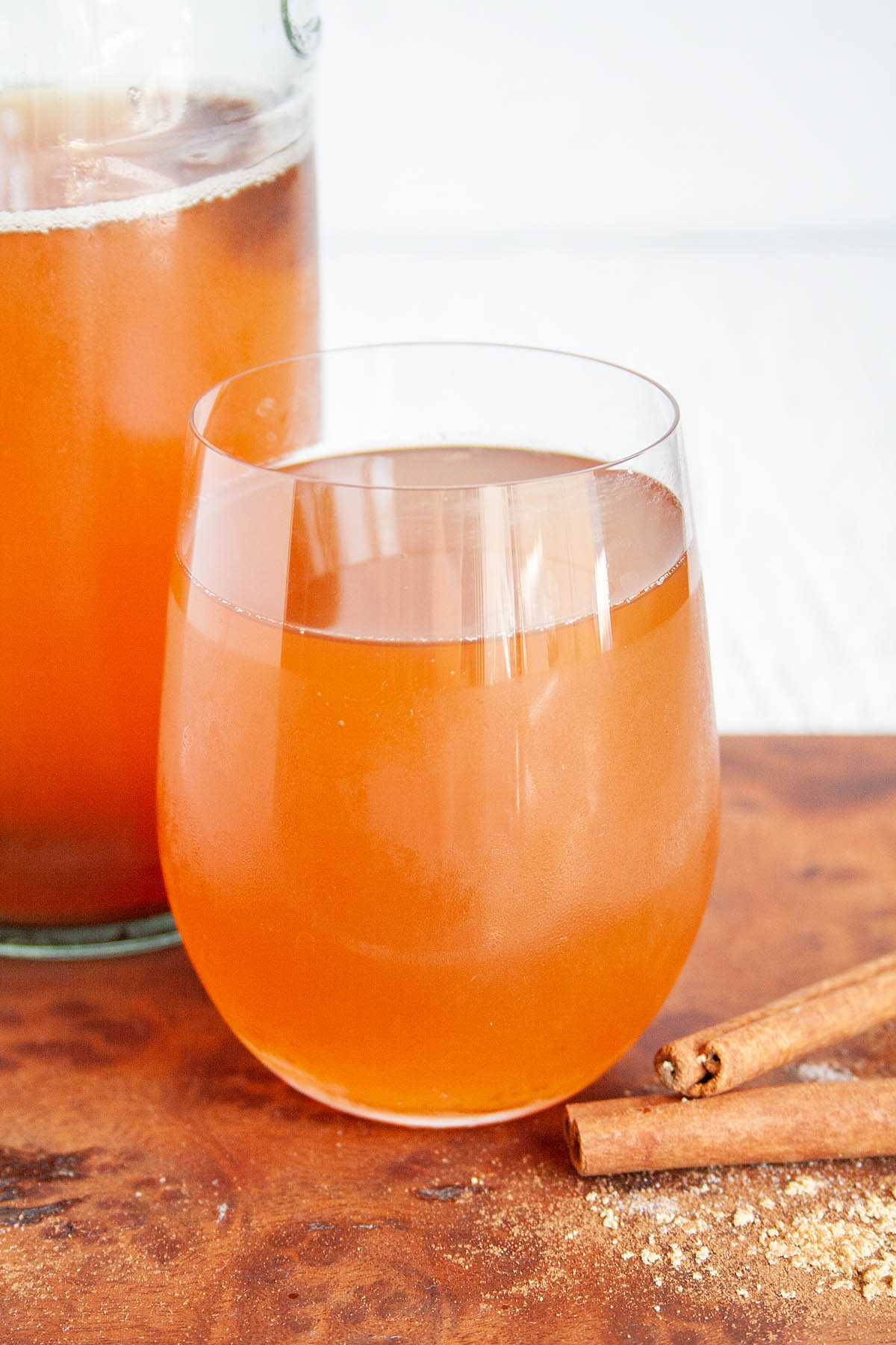 Spiced Kombucha in a wine glass with bottle and cinnamon sticks.