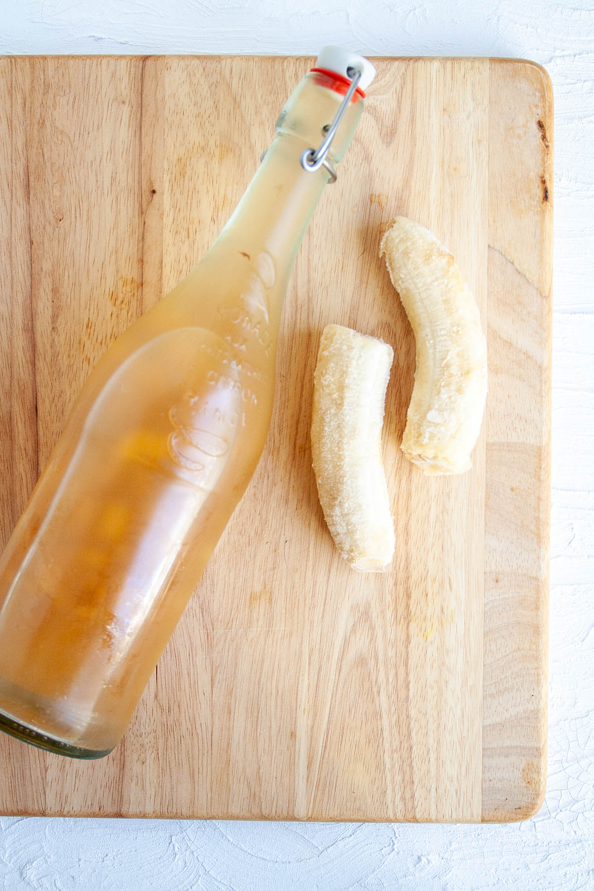 Banana Kombucha in bottle with banana on cutting board.