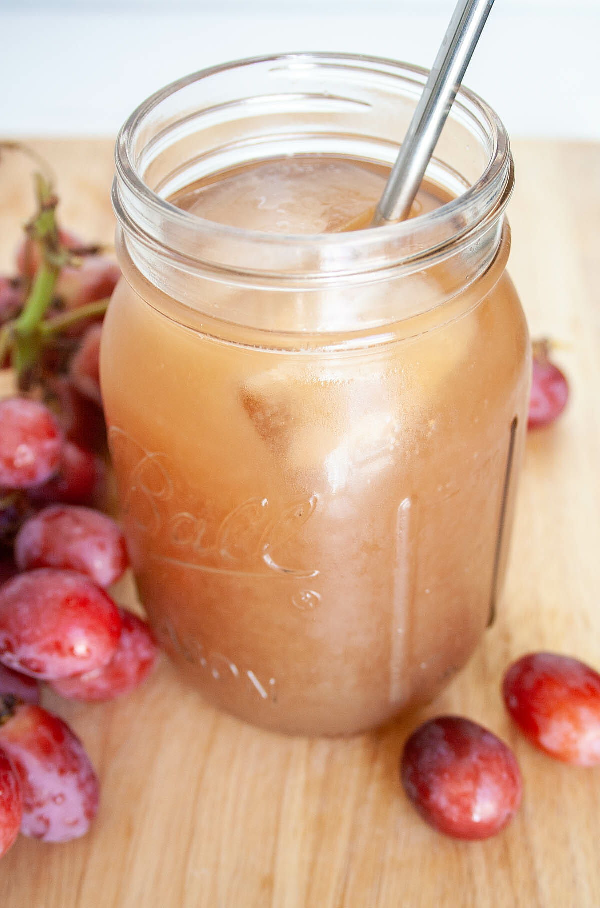 Grape Kombucha in mason jar with a straw.