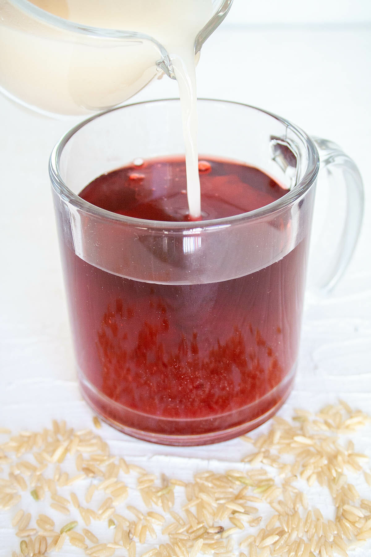 Rice Milk being poured into a mug of hibiscus tea.