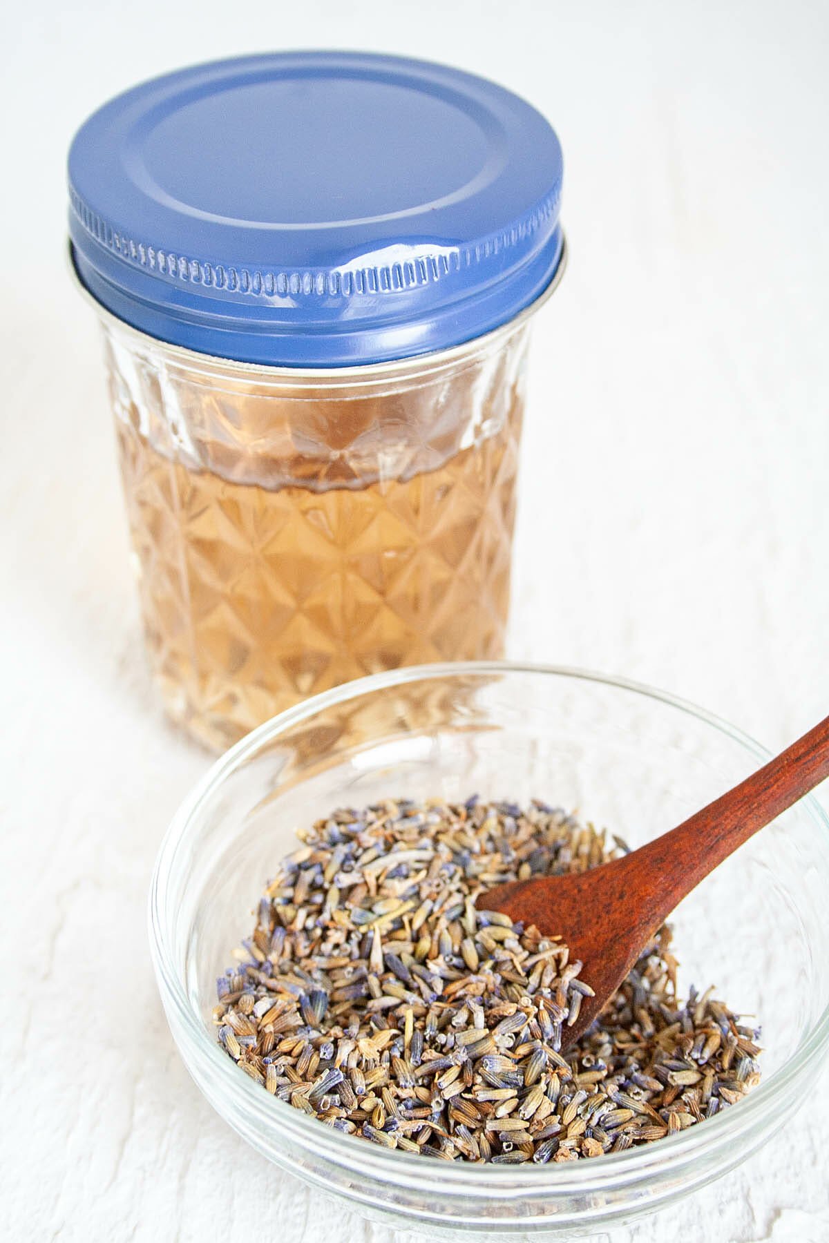 Lavender Simple Syrup in mason jar with lavender buds in a bowl in the foreground.