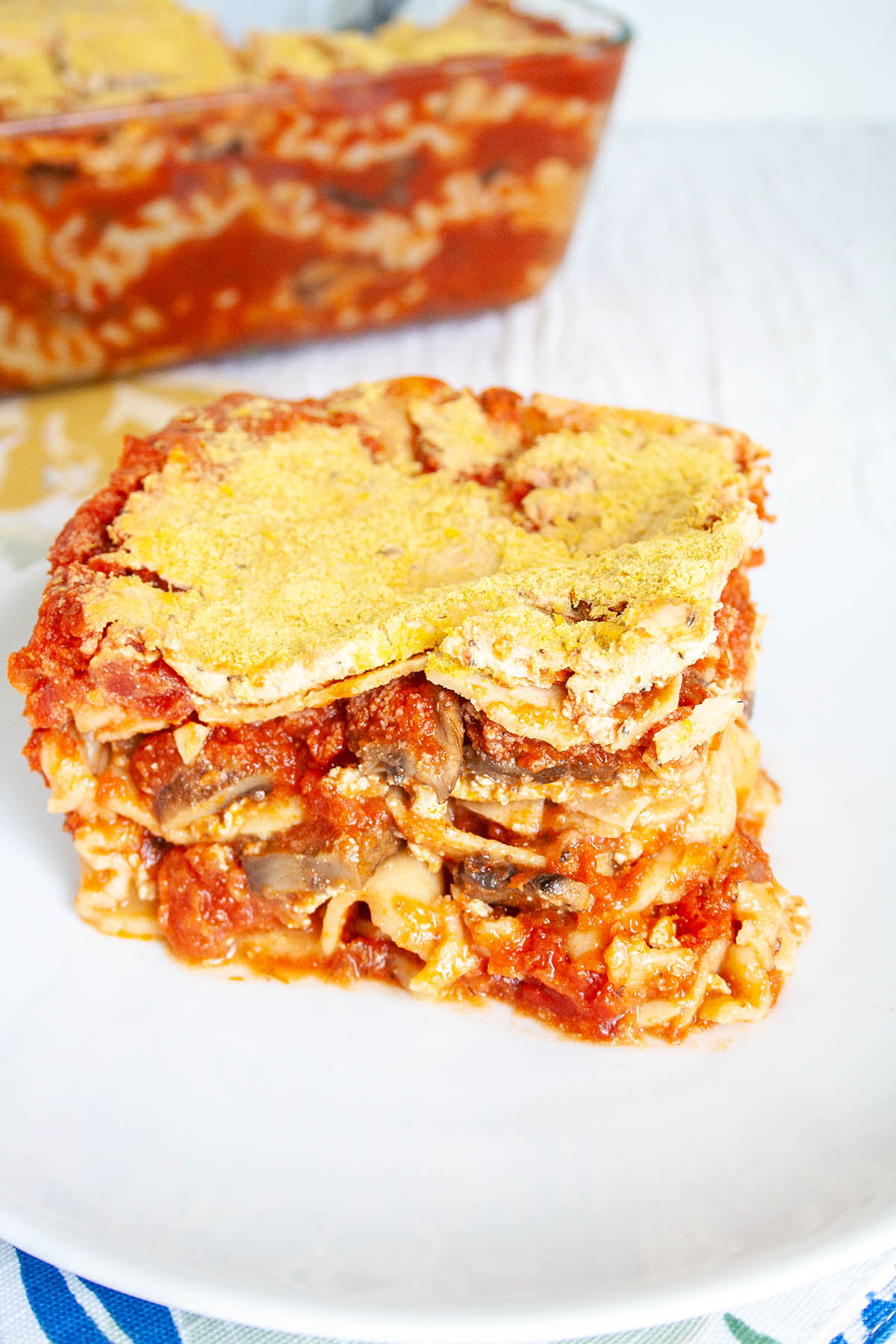 Slice of Vegan Mushroom Lasagna on plate with the rest in baking dish in the background.