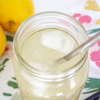 Vanilla Lemonade in a glass with straw. Lemons and vanilla bean in the background.