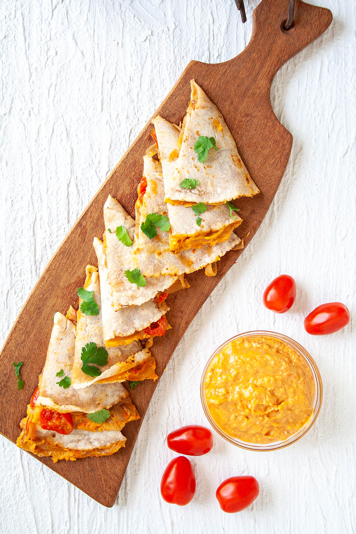 Hummus Quesadilla on cutting board with bowl of hummus and cherry tomatoes.