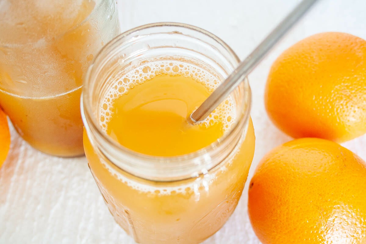Cara Cara Orange Kombucha in mason jar with oranges and bottle of kombucha.