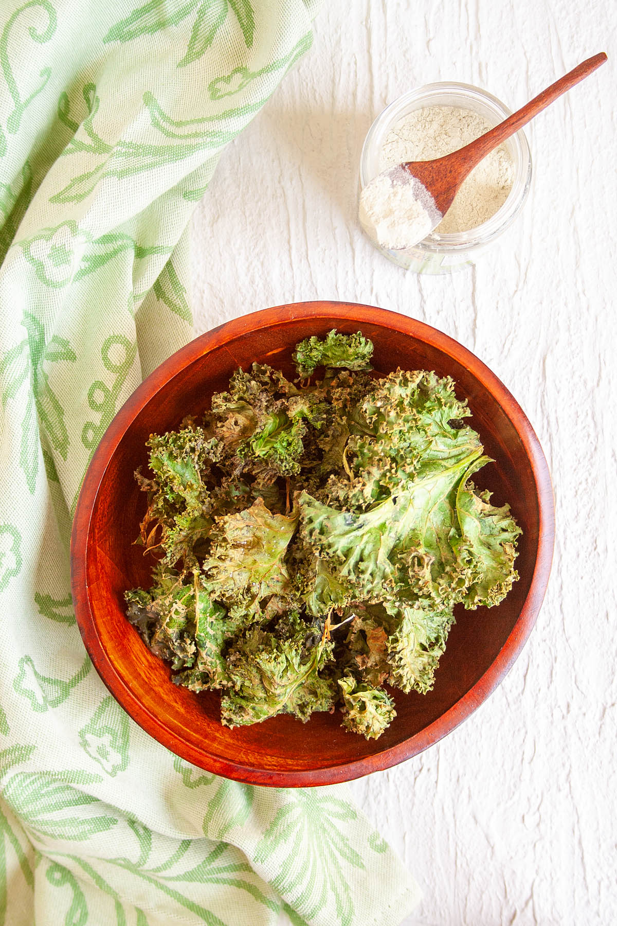 Wasabi Kale Chips in wooden bowl with a jar of wasabi powder.