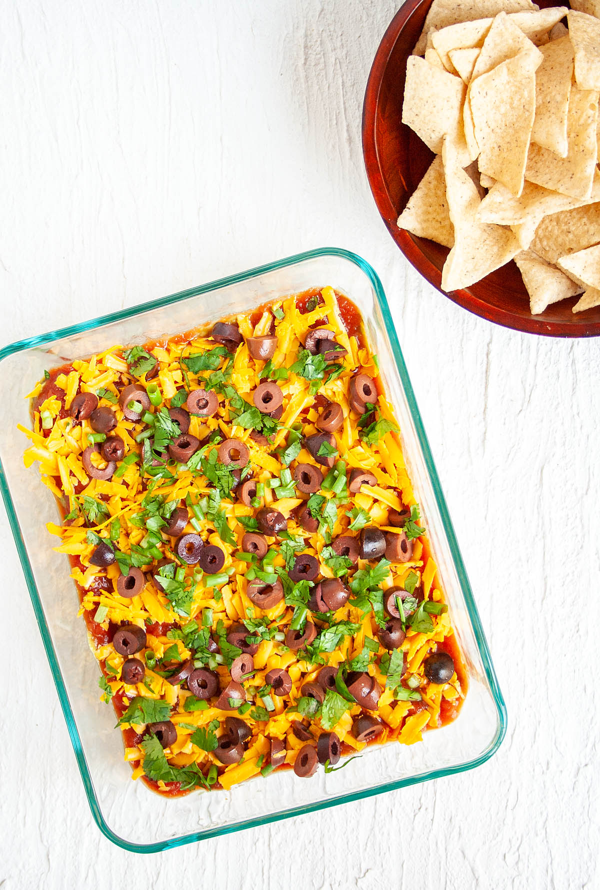 Vegan 7 Layer Dip in baking dish with a bowl of tortilla chips.