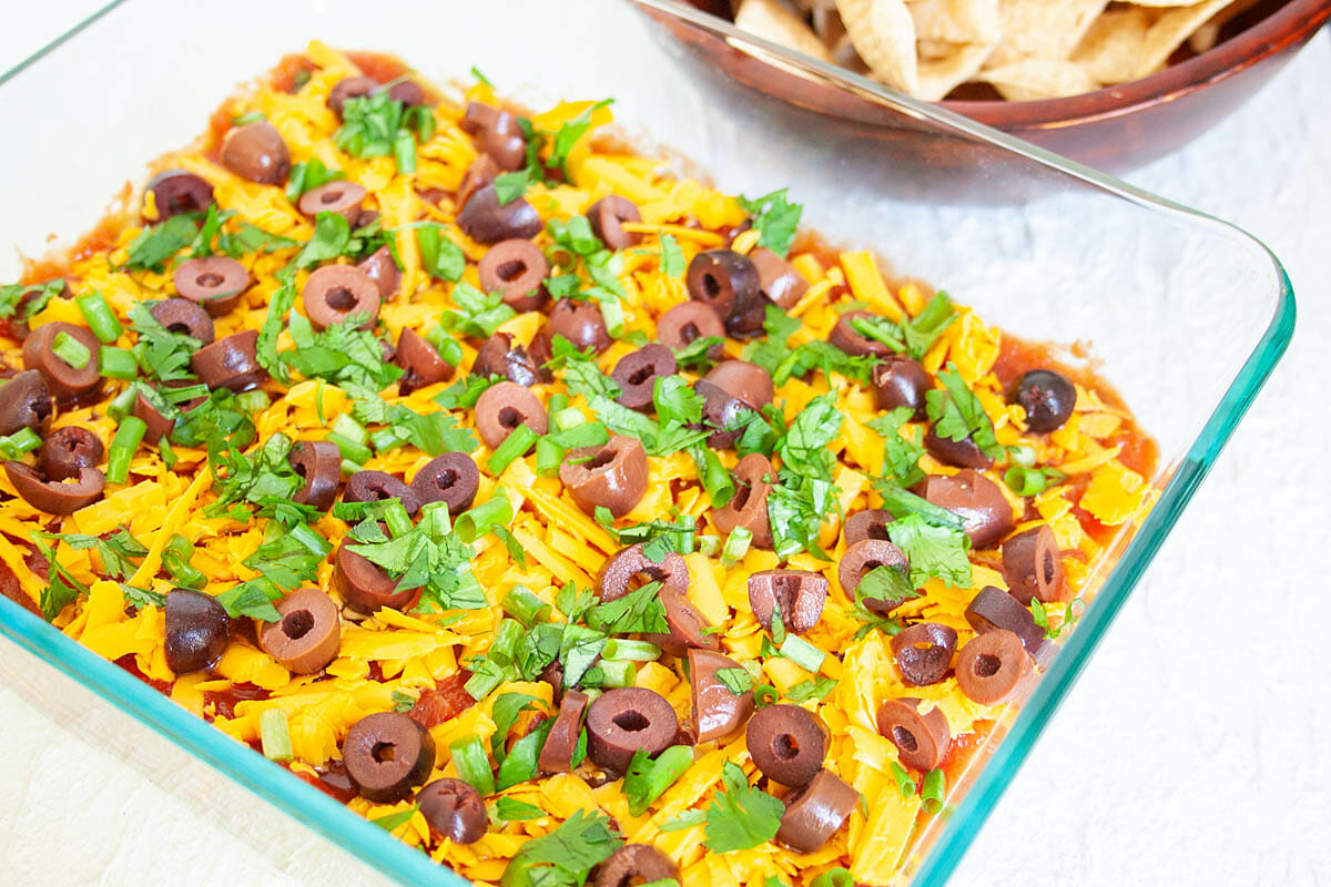 Vegan 7 Layer Dip in a baking dish with tortilla chips in the background.