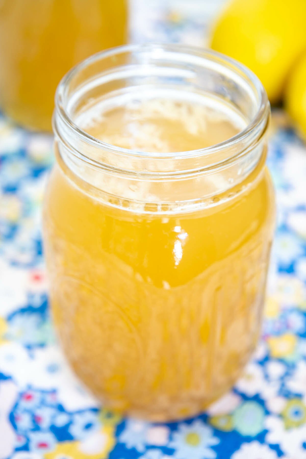 Lemon Green Tea Kombucha in mason jar with a bottle of kombucha and lemons in the background.