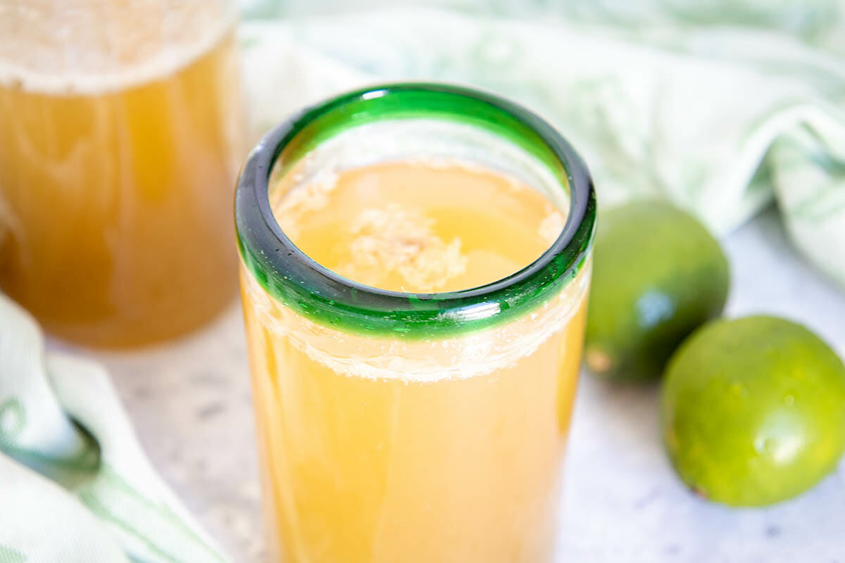 Sweetened with maple syrup, this fizzy Lime Green Tea Kombucha has the perfect balance of sweet and tart flavors. It's an easy DIY recipe! Lime Green Tea Kombucha in glass with limes and a bottle of kombucha in the background.