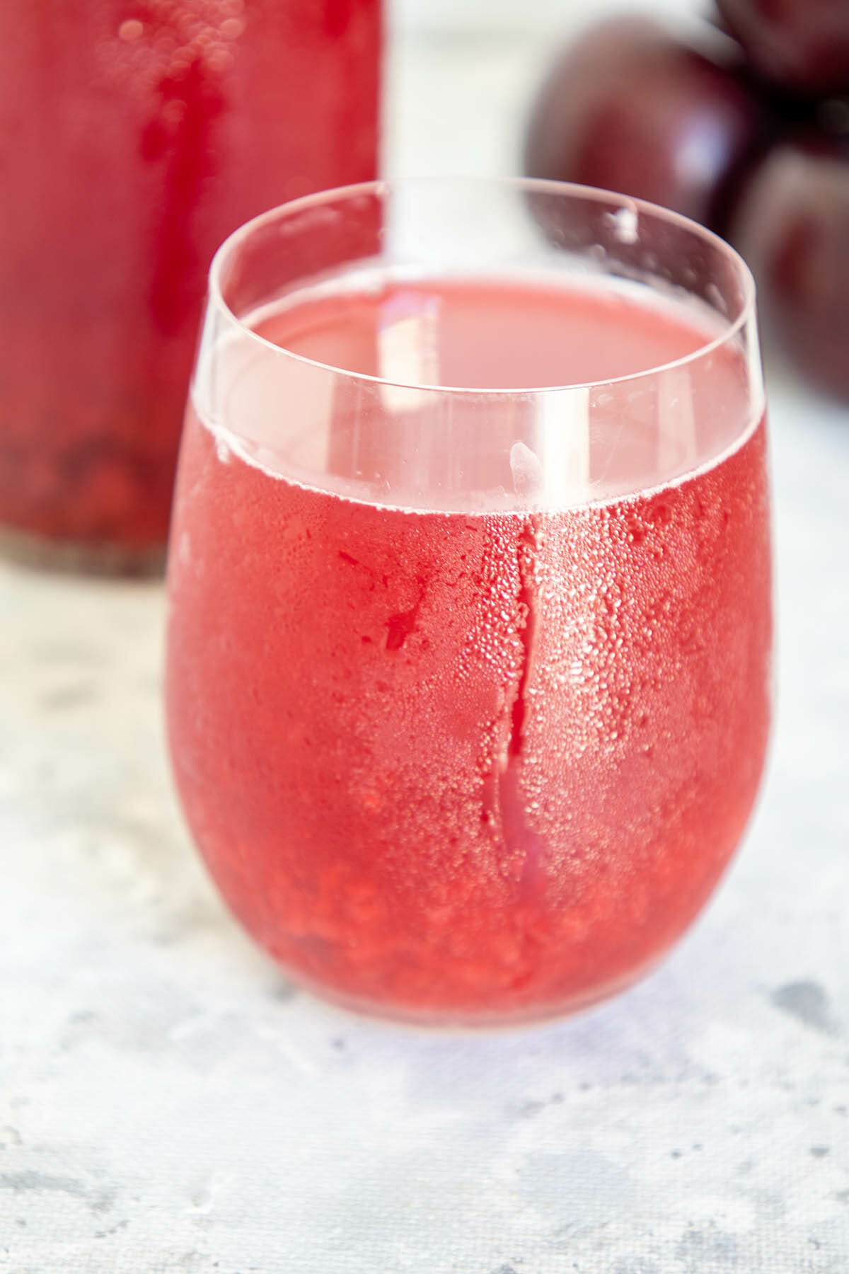 Plum Kombucha in a glass with plums and bottle in the background.