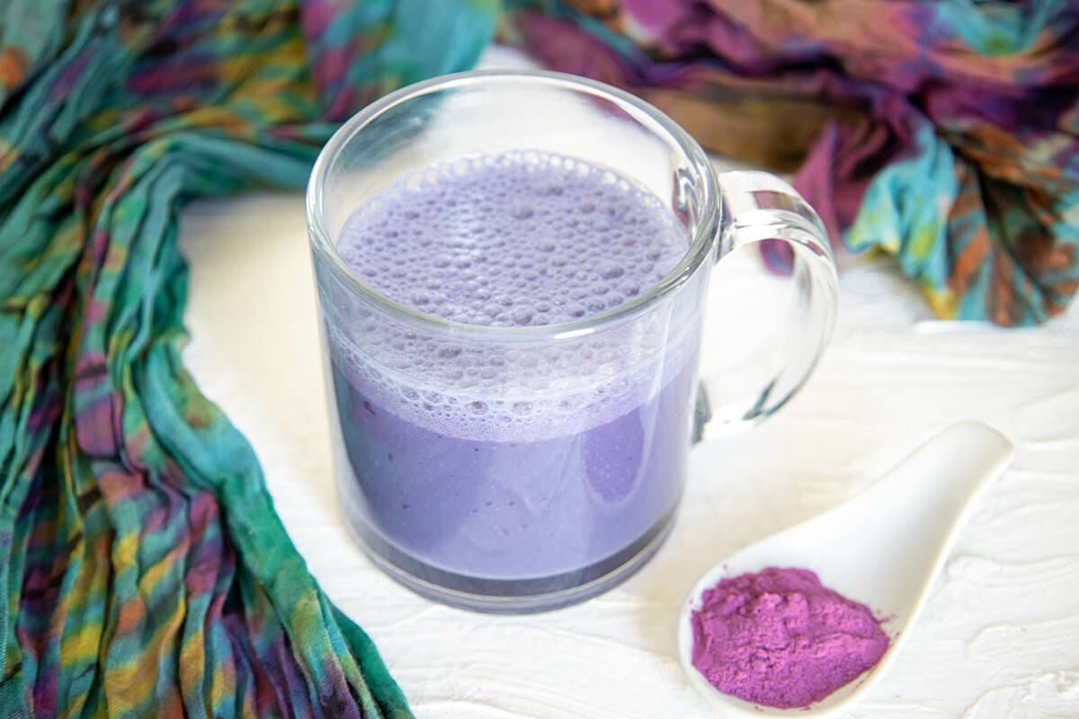 Purple Potato Latte in a mug next to a spoonful of purple potato powder.