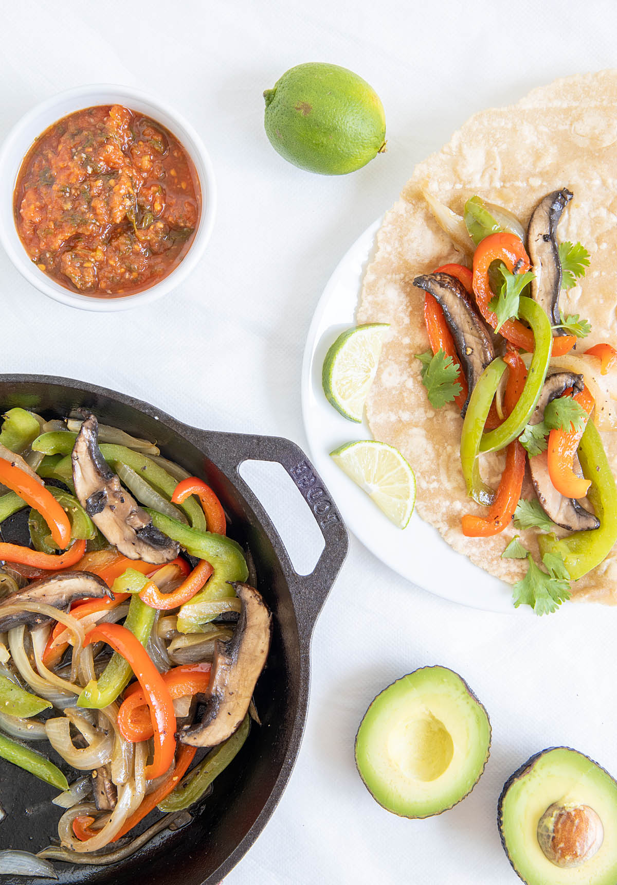 Portobello Fajitas in a skillet and on a plate with salsa, lime, and avocado.