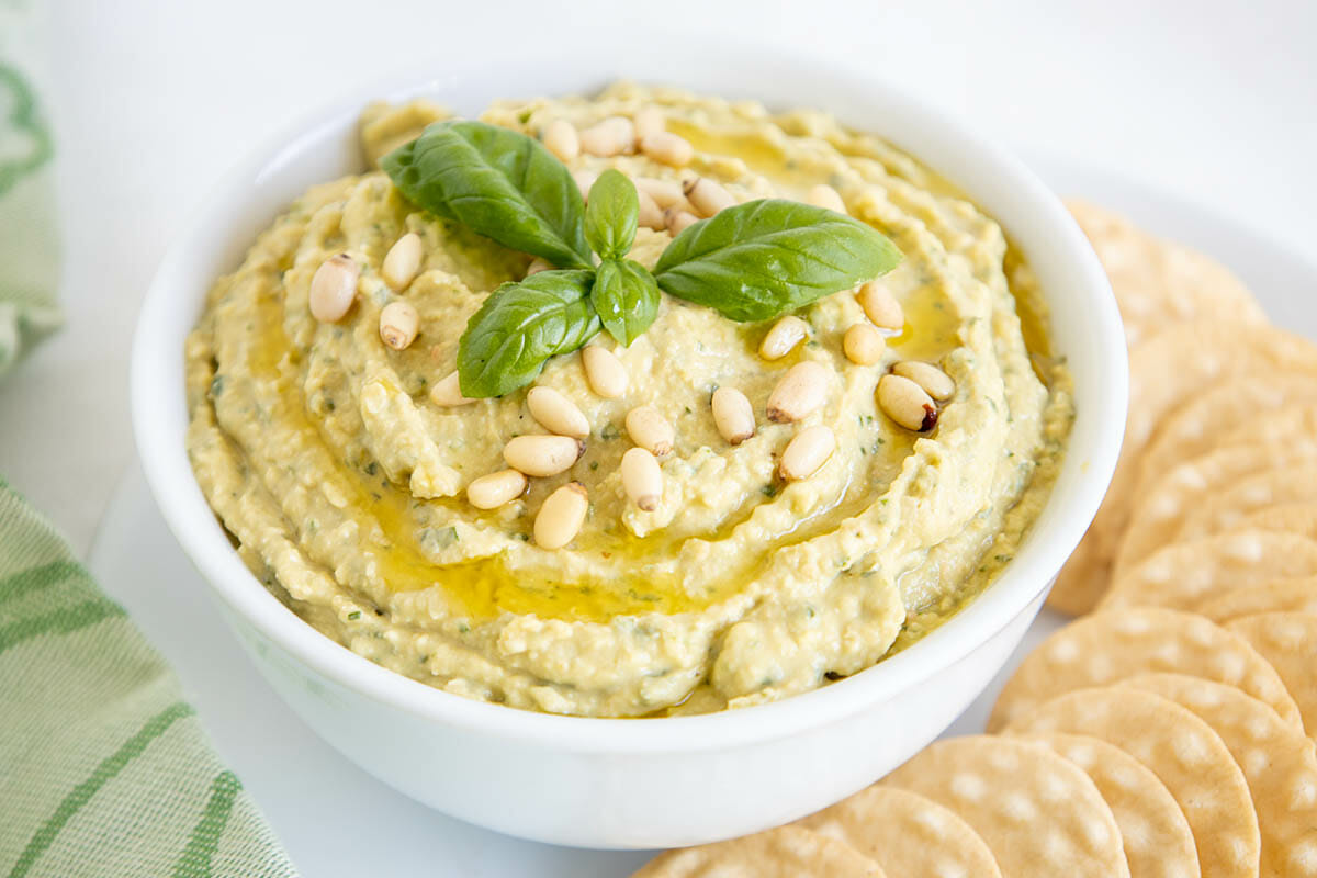 Basil Pesto Hummus in a bowl next to crackers.