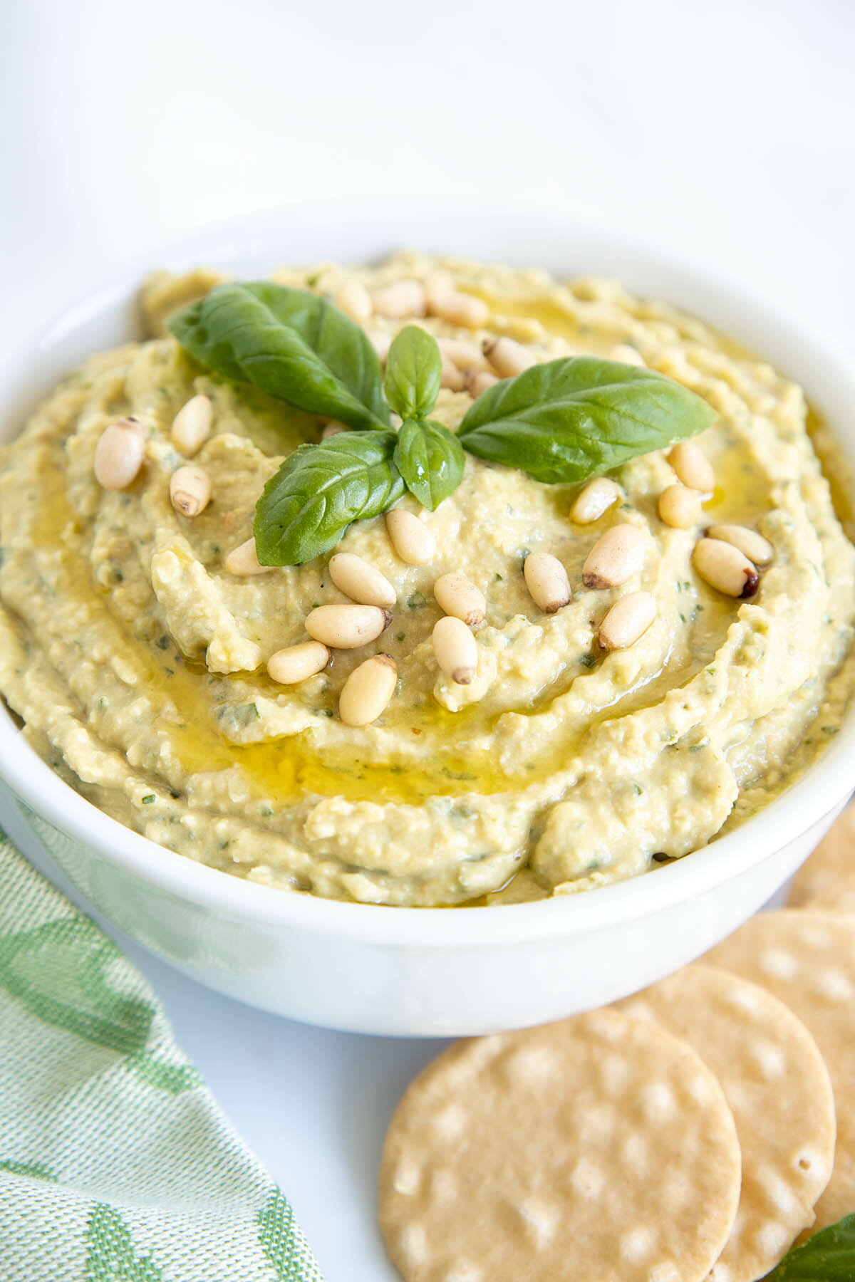 Basil Pesto Hummus in a bowl with crackers on a plate.