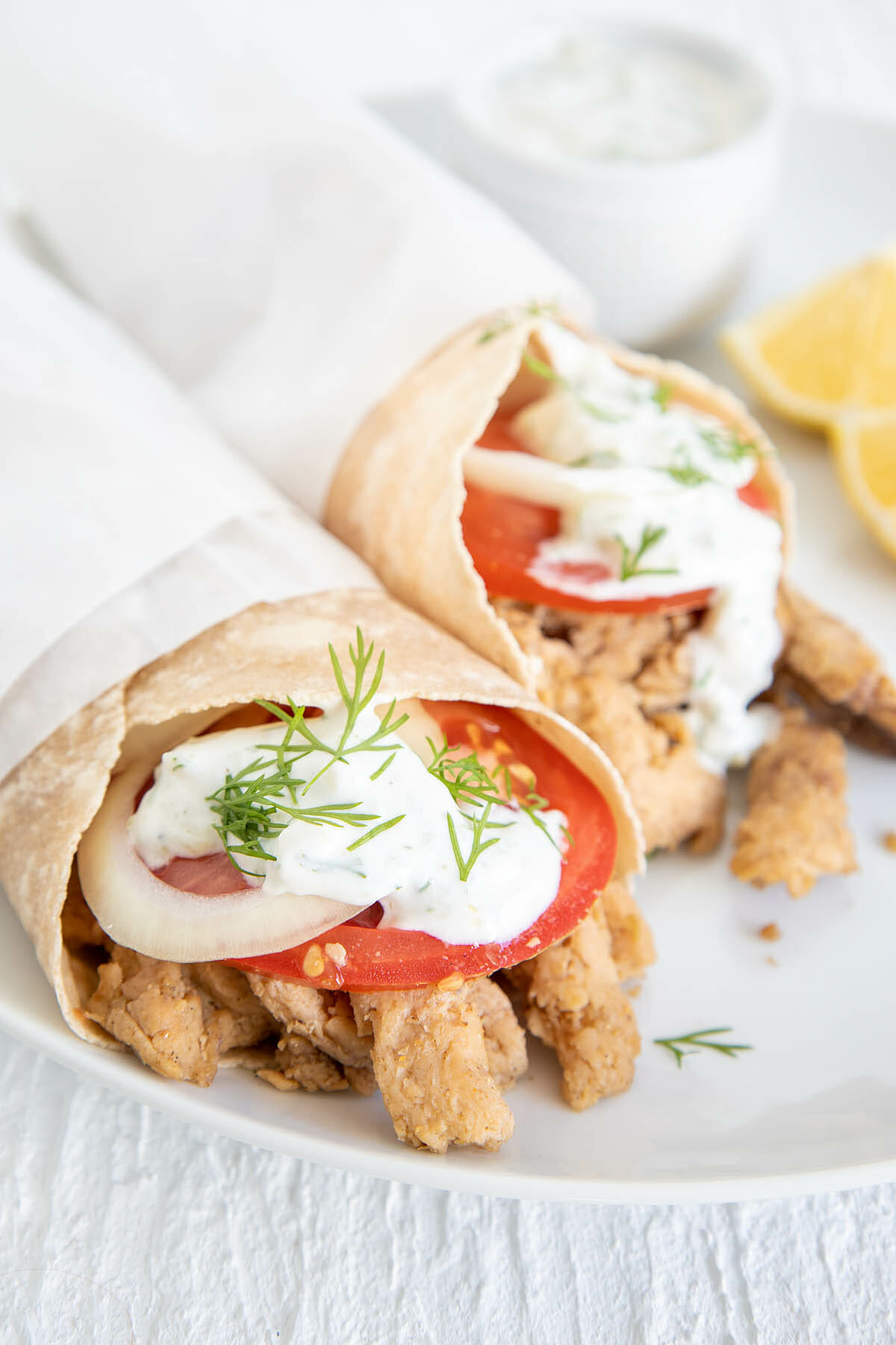 Vegan Gyros on a plate with tzatziki and lemon wedges.