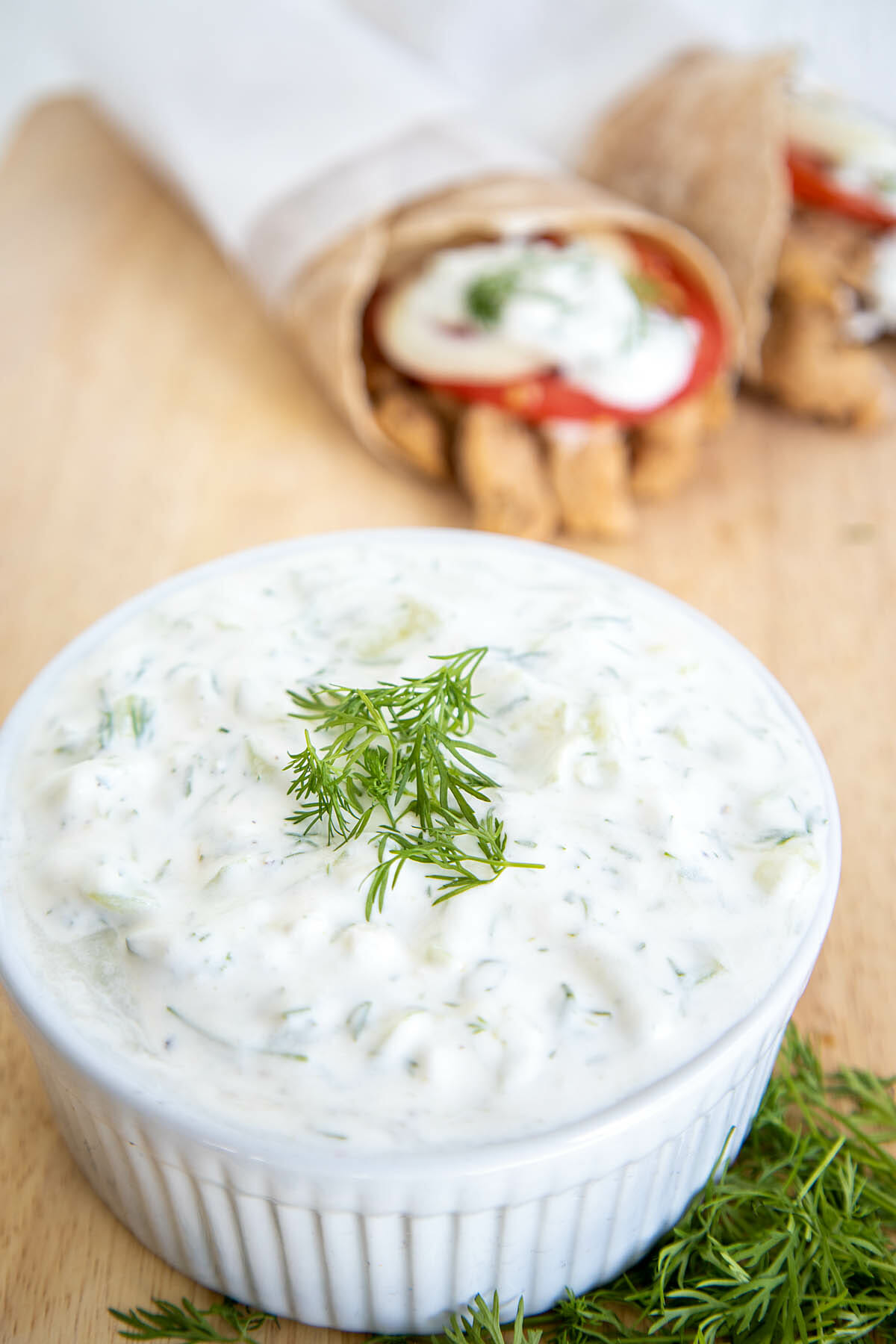 Vegan Tzatziki next to dill with vegan gyros in the background.