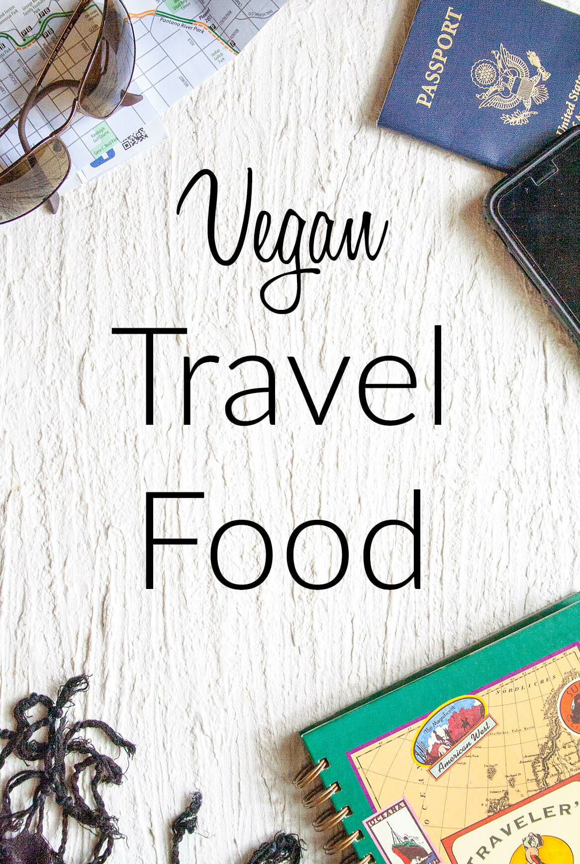 Sunglasses, map, passport, phone, scarf and travel journal on a white background with the text, "Vegan Travel Food" written on it.