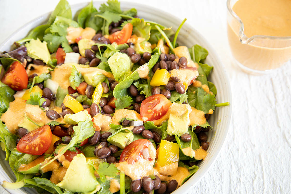 Vegan Southwest Salad in a bowl with pitcher of chipotle dressing.