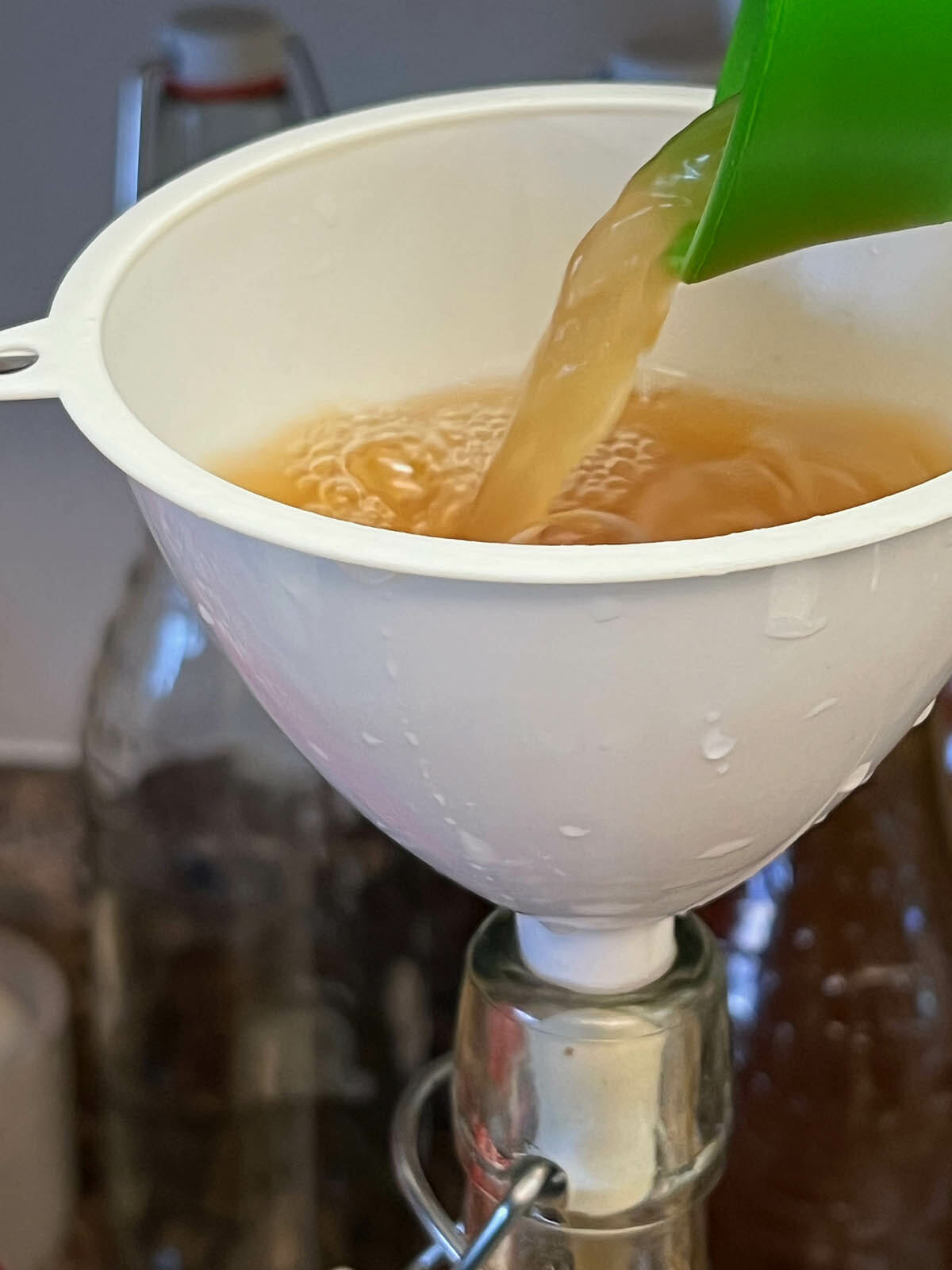 Kombucha being poured into a funnel into bottle.
