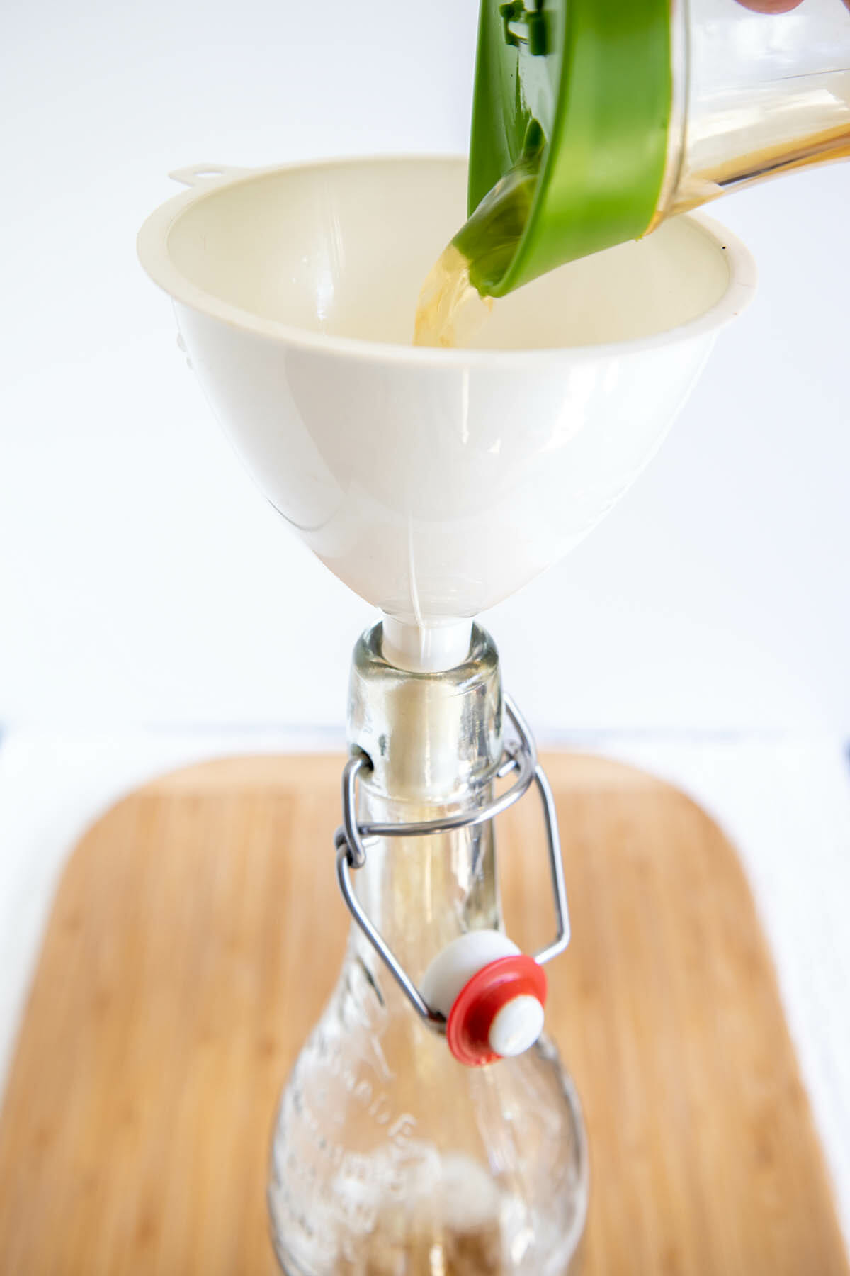 Green tea kombucha being poured into a funnel over a bottle.