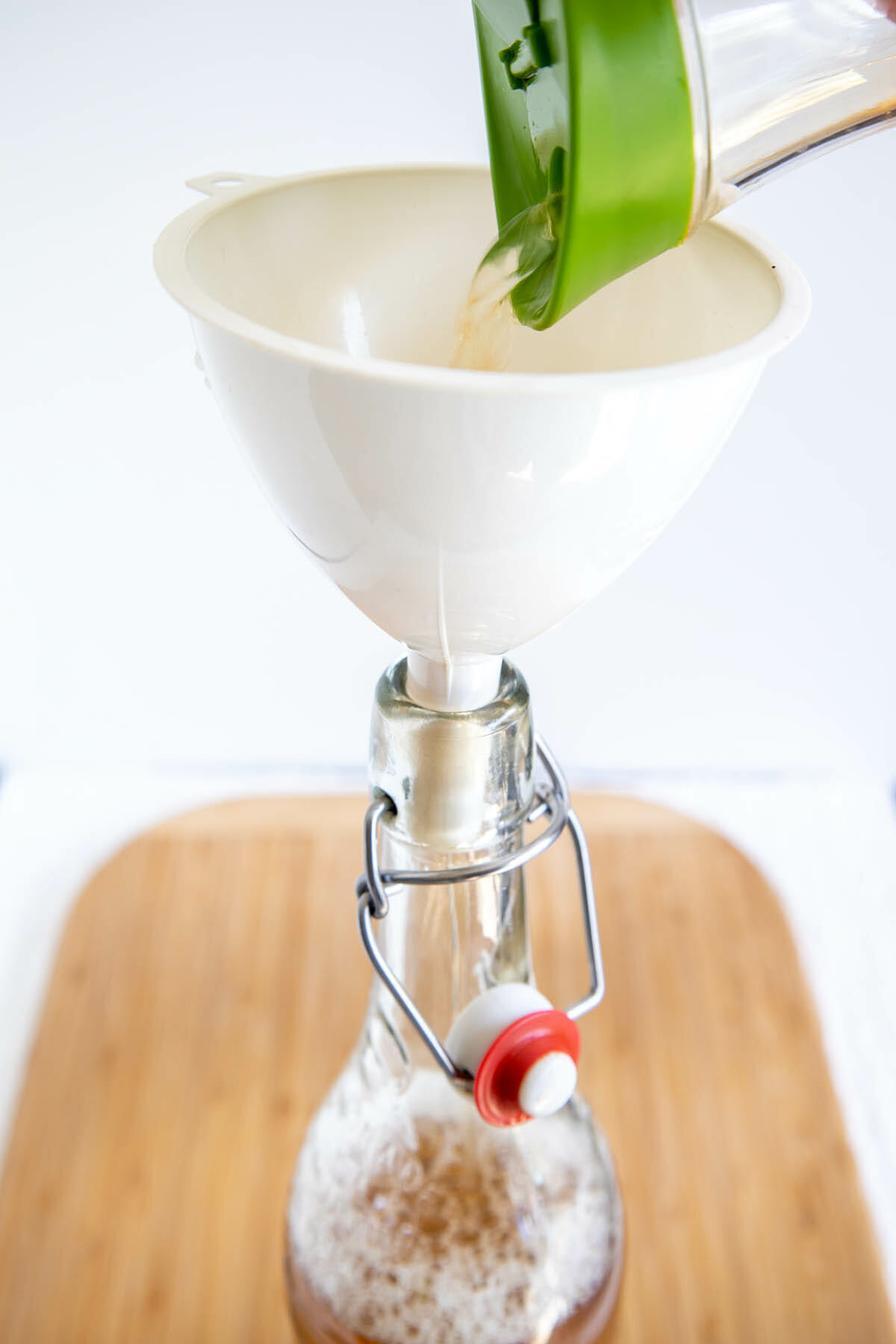 Kombucha being poured into a funnel over a bottle that has the coffee mixture in it.