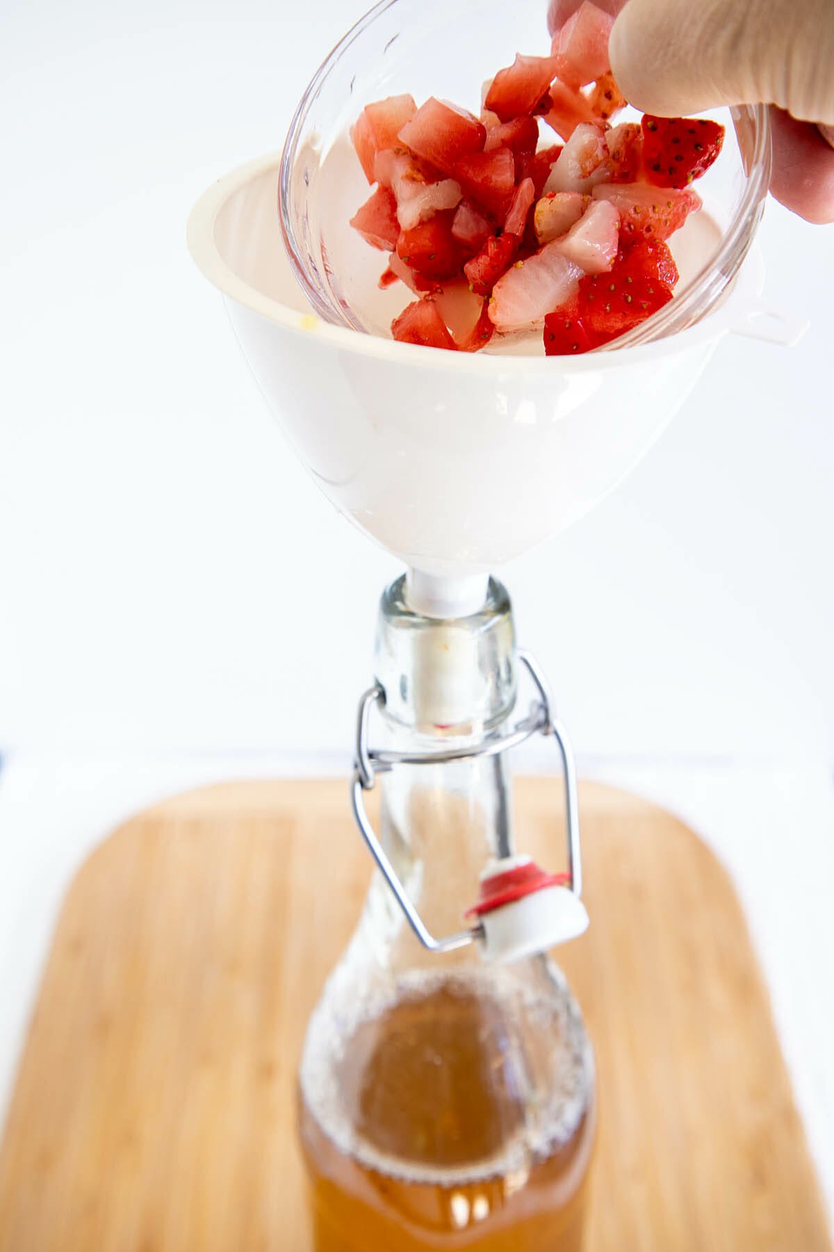 Chopped strawberries being poured into a funnel over a bottle.