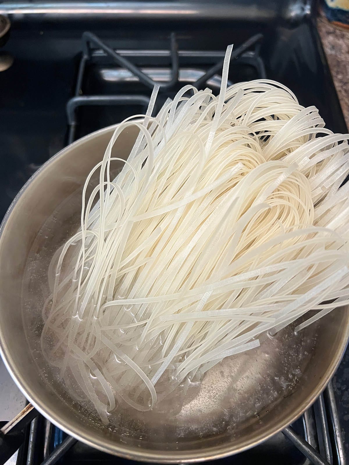 Rice noodles being added to a saucepan with boiling water.