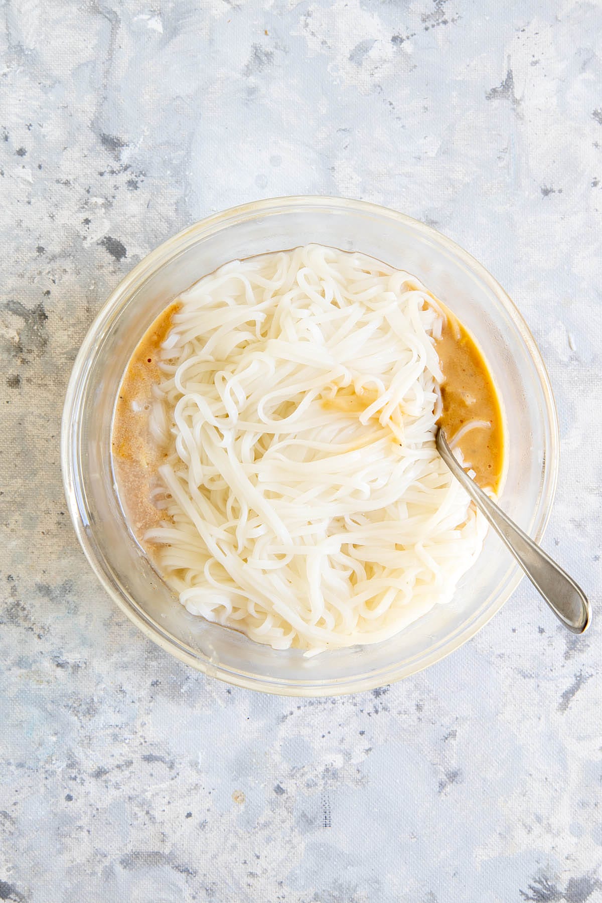 Rice noodles added to tahini sauce in a bowl.