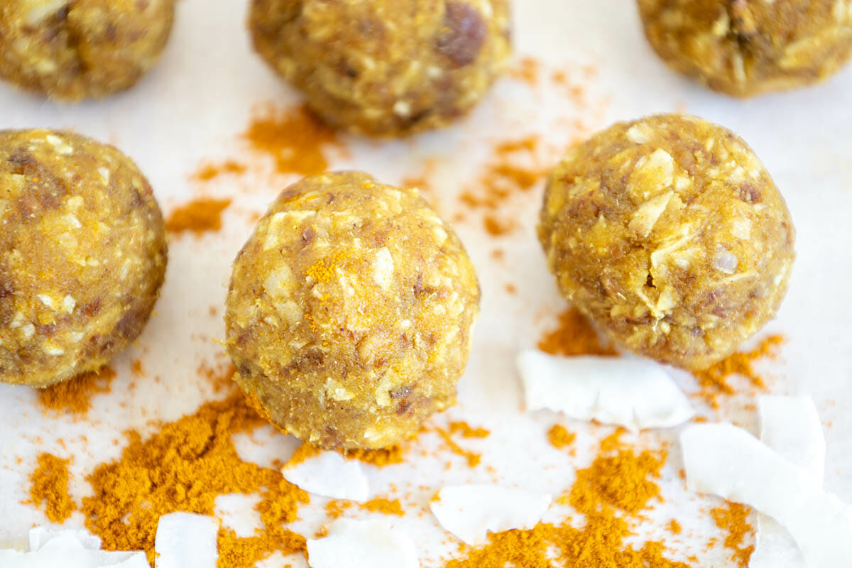 Turmeric Energy Balls on parchment paper with turmeric and sliced coconut.