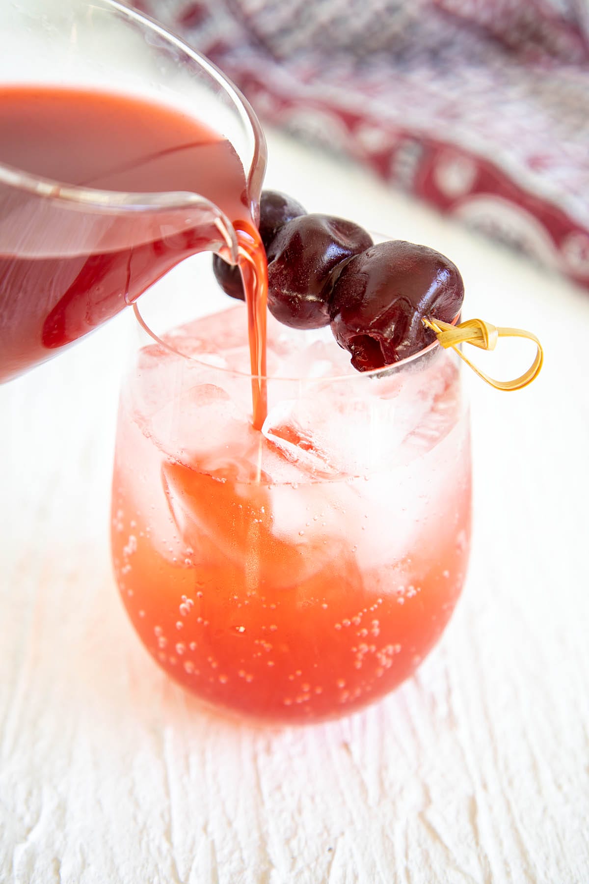 Tart Cherry Shrub being poured into a glass with club soda and ice cubes.