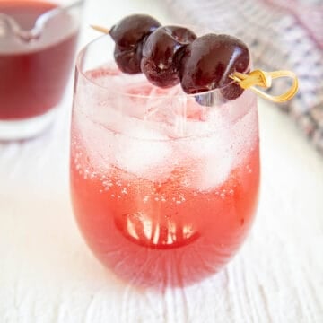 Cherry Shrub in a glass with club soda and a pitcher in the background.