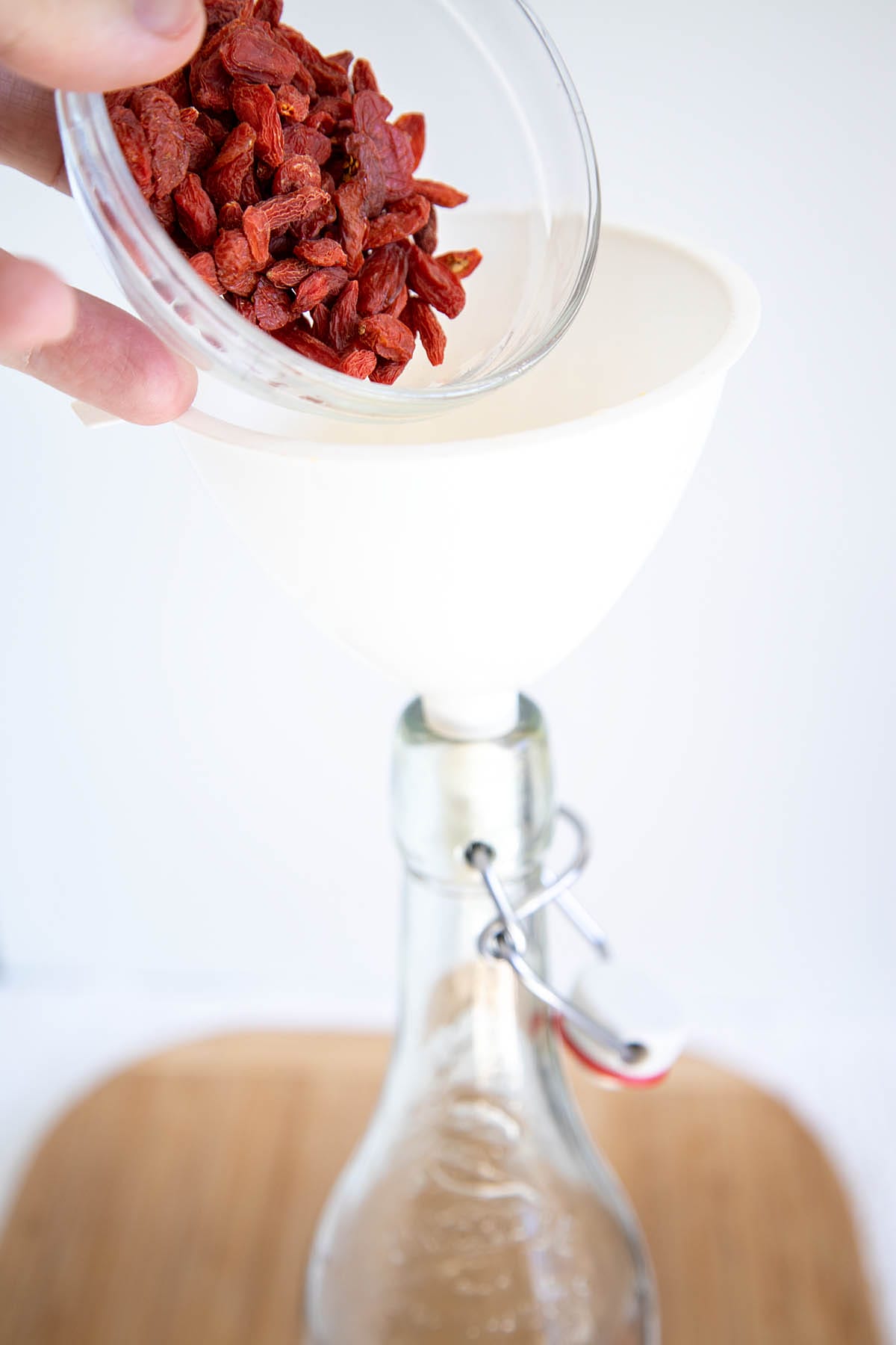 Goji berries being poured into a funnel into a bottle.