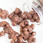 Chocolate chips spilling out of a mason jar onto parchment paper.