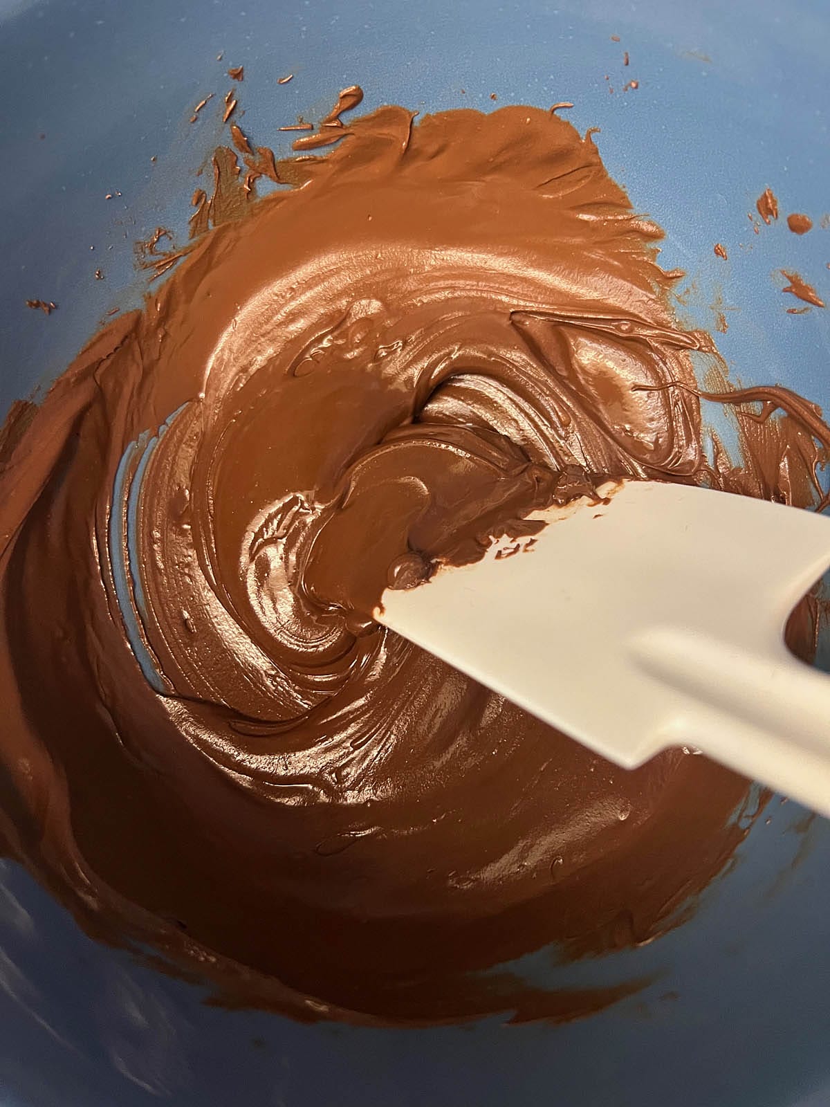 Melted chocolate in a large bowl with a rubber spatula.