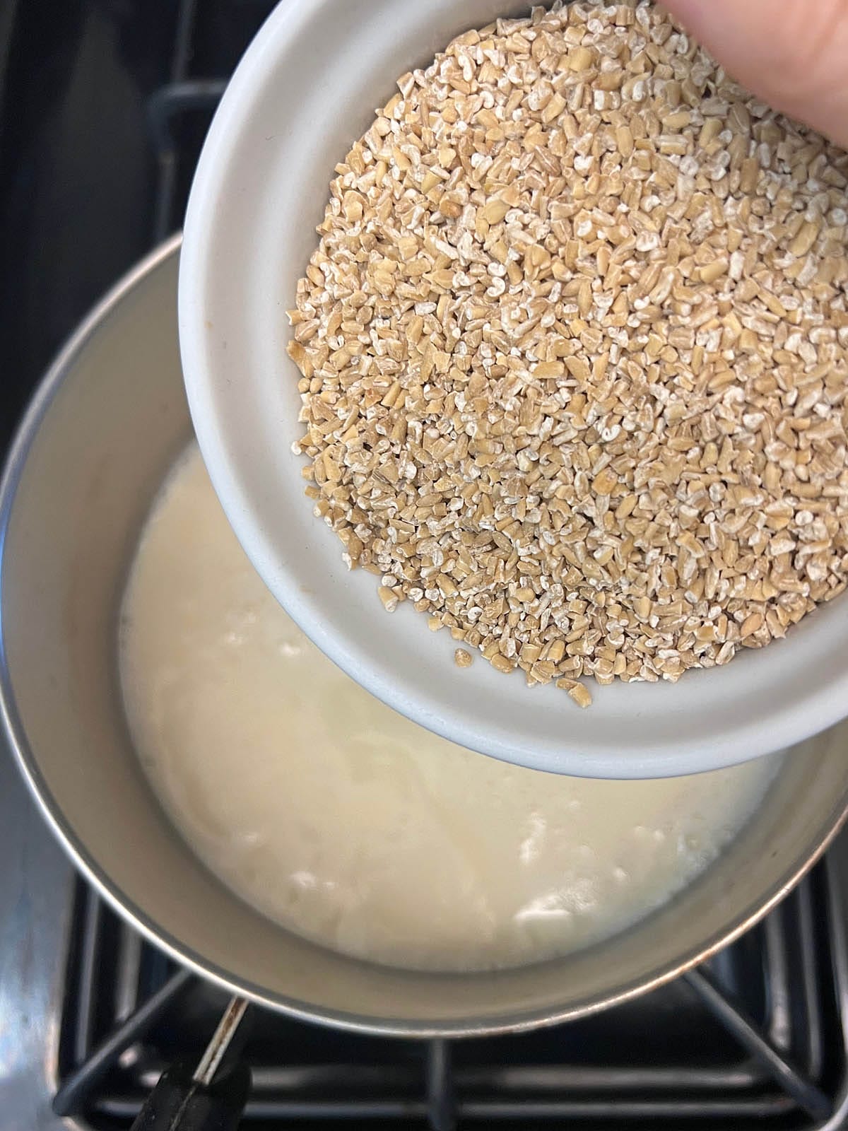 Steel cut oats being poured into saucepan with almond milk.