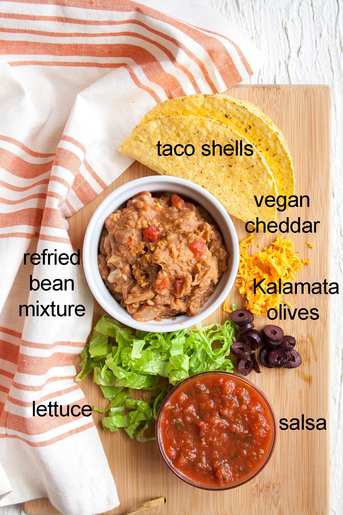 Ingredients for refried bean tacos on a cutting board with labels.