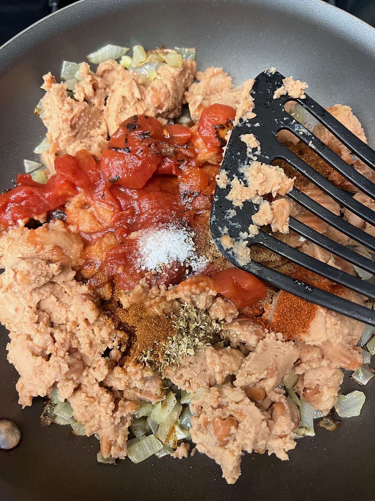 Refried beans, diced tomatoes, spices, and vegan cheddar added to the skillet.
