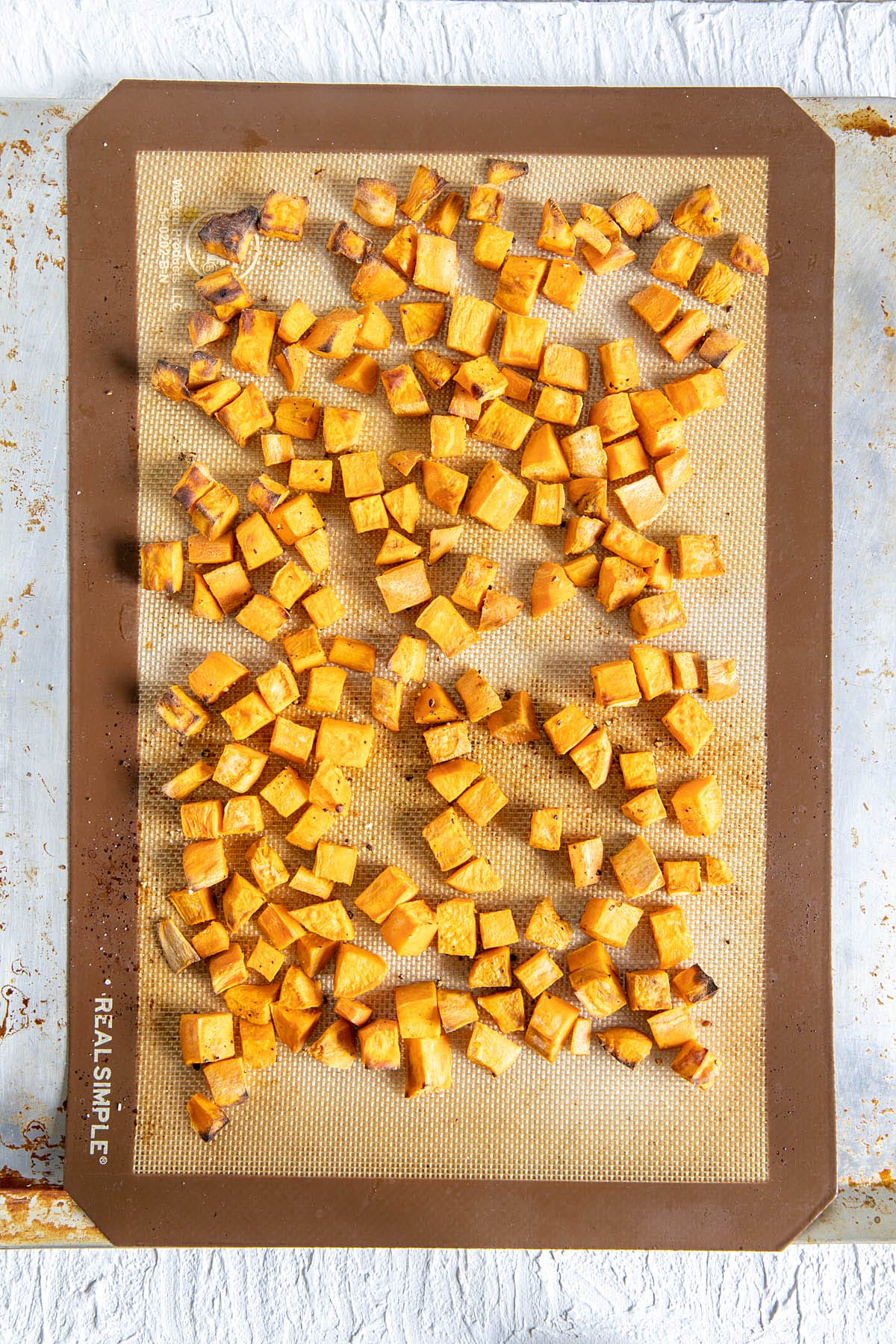 Roasted sweet potato cubes on a silicone mat on a baking sheet.