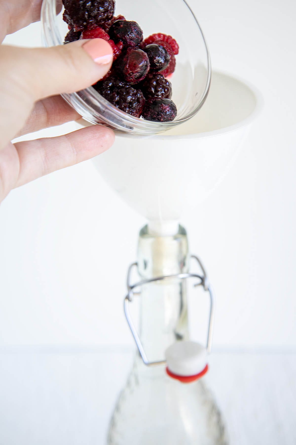 Mixed berries being poured into a funnel into a bottle.