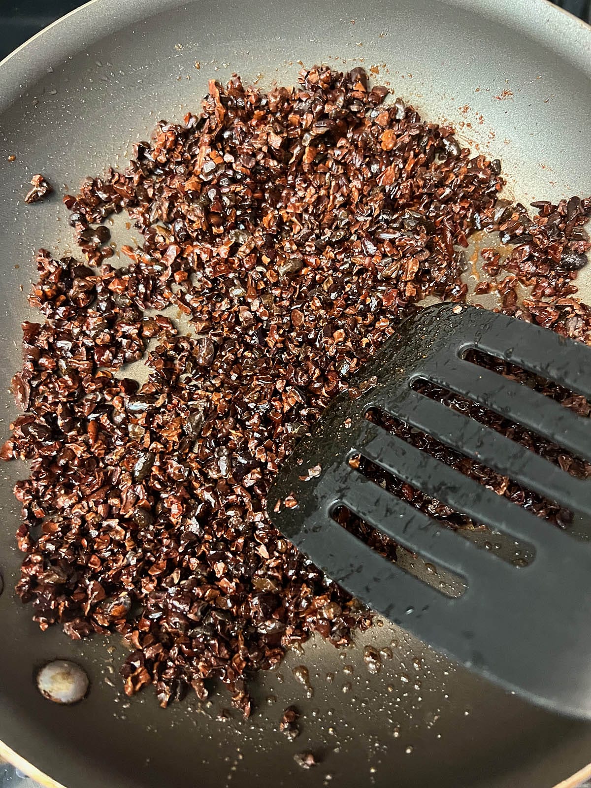 Cooked caramelized cacao nibs in a skillet with spatula.