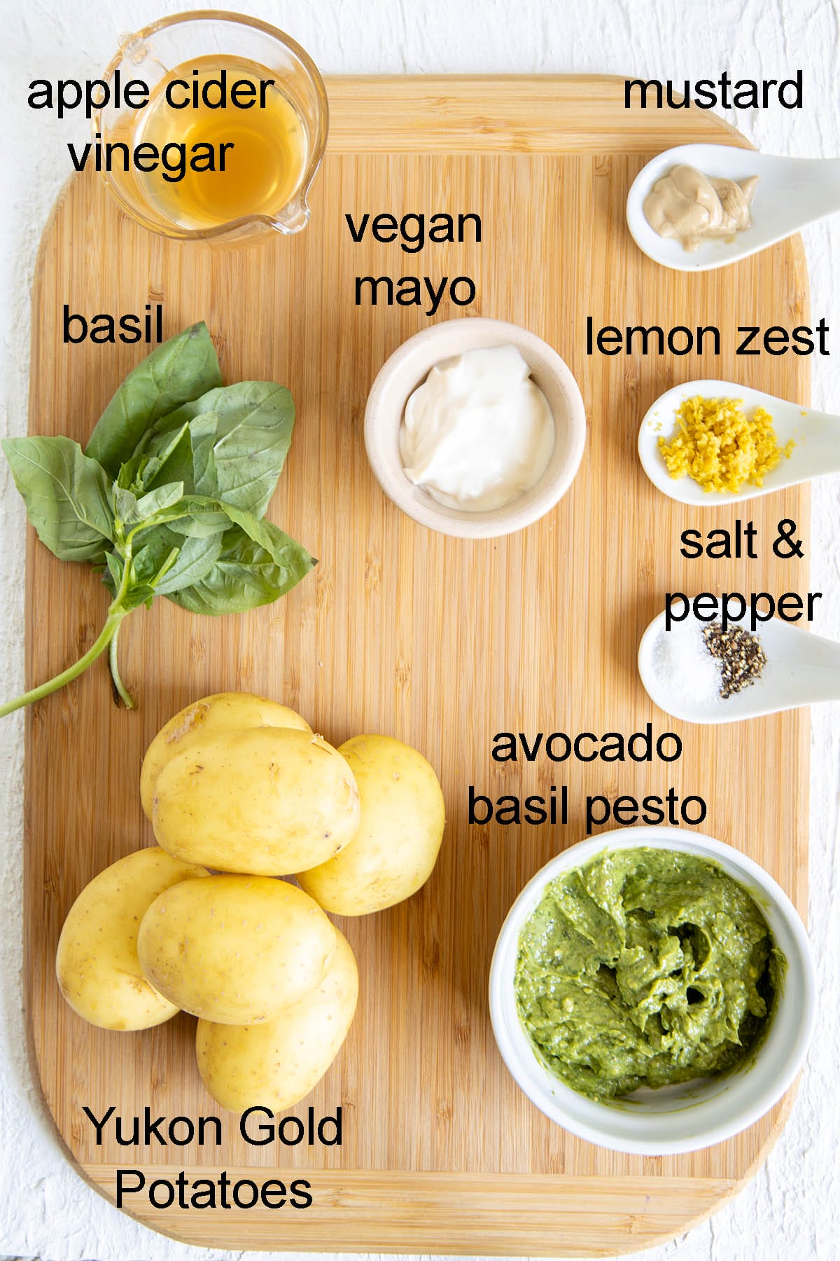 Avocado pesto potato salad ingredients on a cutting board with labels.