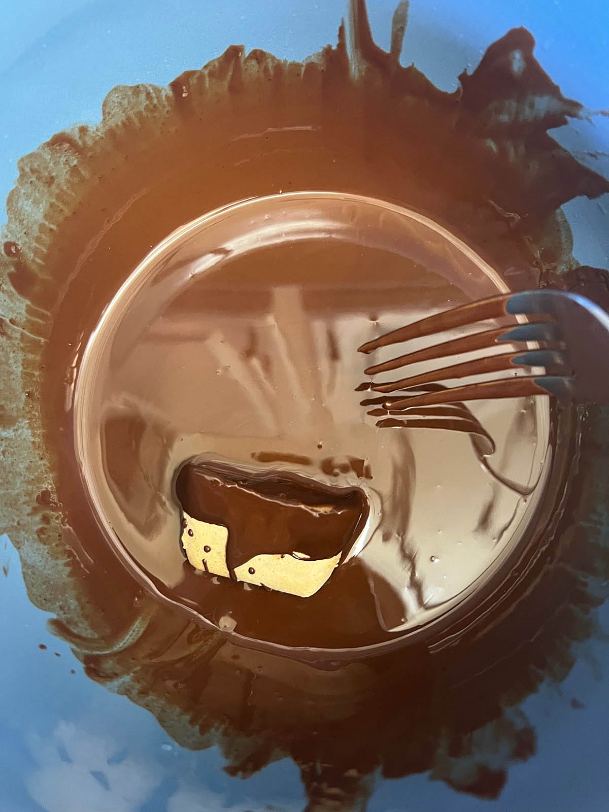 Frozen peanut butter bite in bowl of melted chocolate with fork.