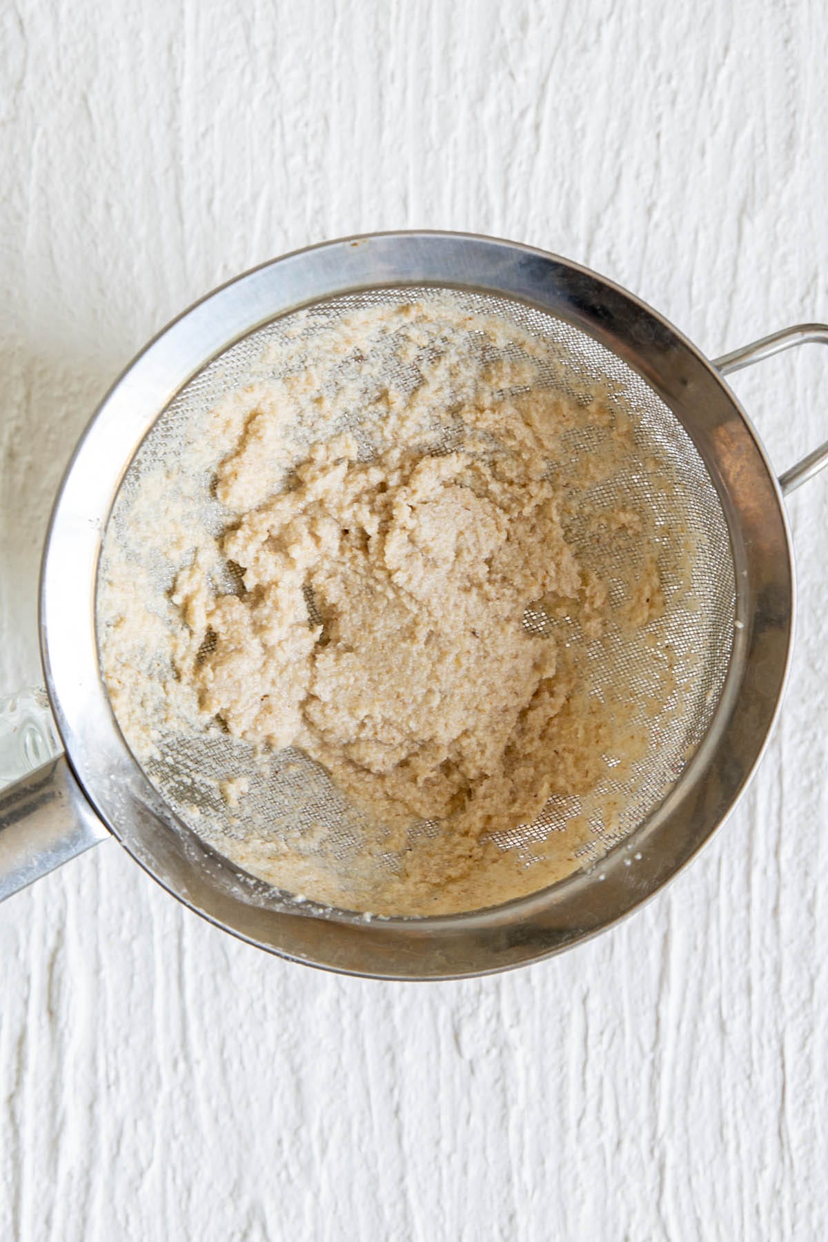 A fine mesh strainer with walnut pulp.