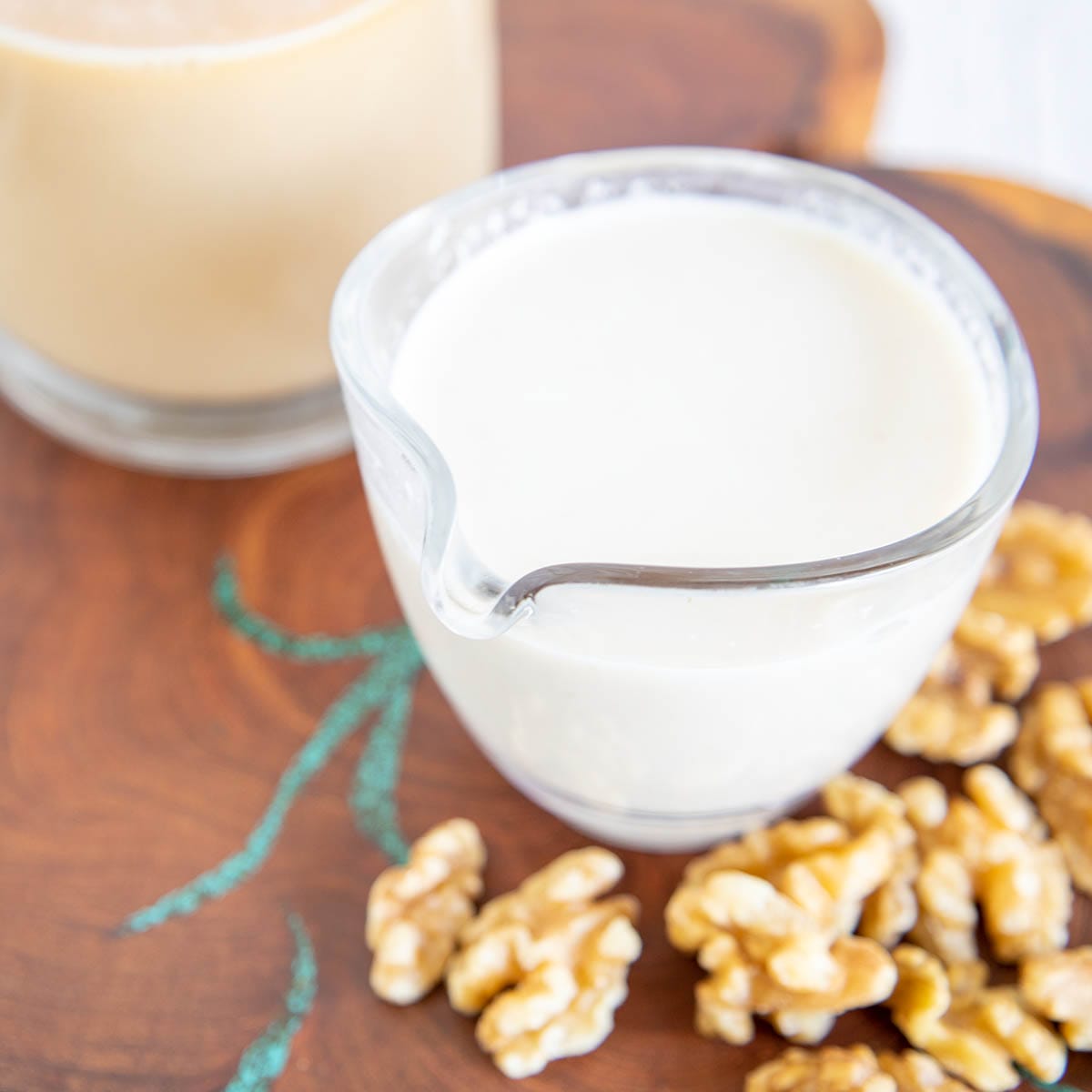 Homemade Walnut Milk in a pitcher with a mug of tea in the background.